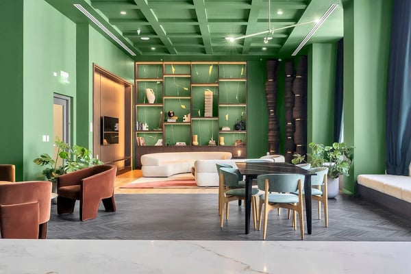 Modern lounge with green walls, wooden shelving unit, cream curved sofa, terracotta armchairs, black dining table, and potted plants
