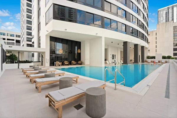 Rooftop resort pool at dusk with illuminated city skyline, lounge seating, and sunset sky