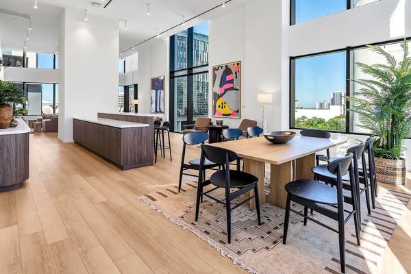Modern open-plan living space with wooden dining table, black chairs, kitchen island, and floor-to-ceiling windows overlooking city skyline